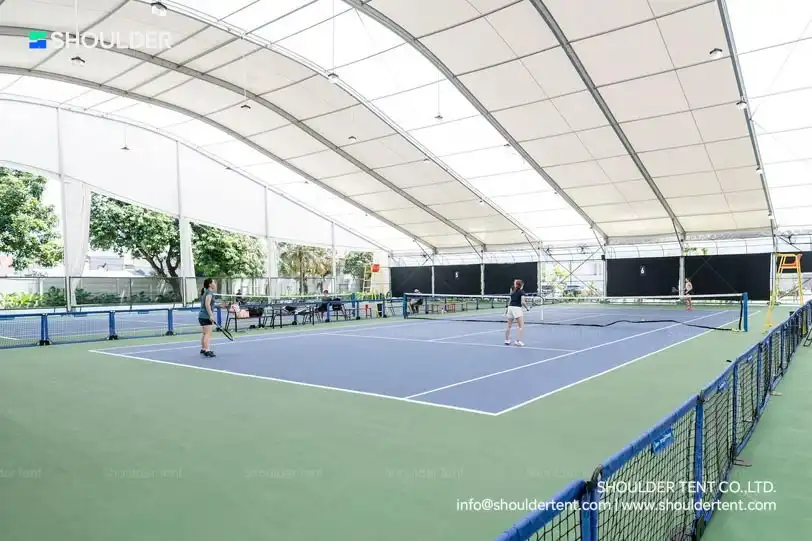 Indoor tennis courts under a large aluminum clear span curved roof structure.